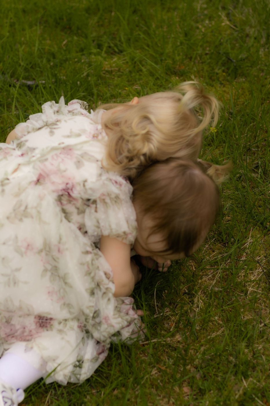 To små søstre i blomsterkjole liggende i gresset, fotografert av Josefine Bergstrøm